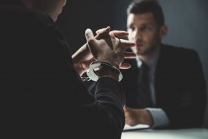 Investigator faces suspect in interview room while suspect back to the viewer and wears handcuffs, JAGMAN investigation, IG Investigation, 15-6 Investigation, OSI Investigation, NCIS Investigation, CID Investigation; find an AR 15-6 investigation lawyer; Find a JAGMAN Investigation lawyer