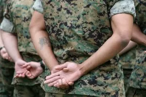 Marines stand at ease in formation with their backs to the photo viewer