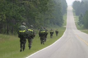 Soldiers on a road march with combat ruck sacks and reflective belts march along a major road that runs through Fort Bragg